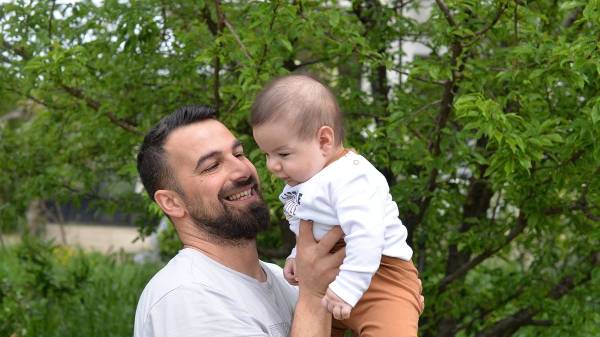 A joyful father lifts his baby in a green, lush outdoor setting.